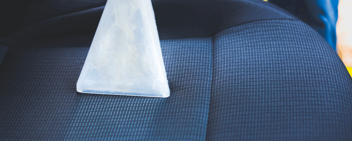 A professional car upholstery cleaning, their machine runs over a deep blue car seat, revealing a lighter blue strip underneath the grime.