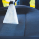 A professional car upholstery cleaning, their machine runs over a deep blue car seat, revealing a lighter blue strip underneath the grime.