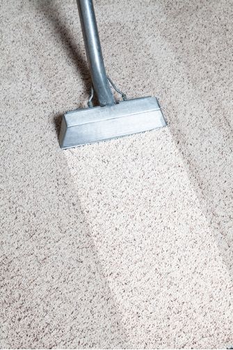 A close-up of a carpet cleaner being used on a beige carpet, revealing the best carpet cleaning results with a visibly clean strip next to the surrounding uncleaned area.